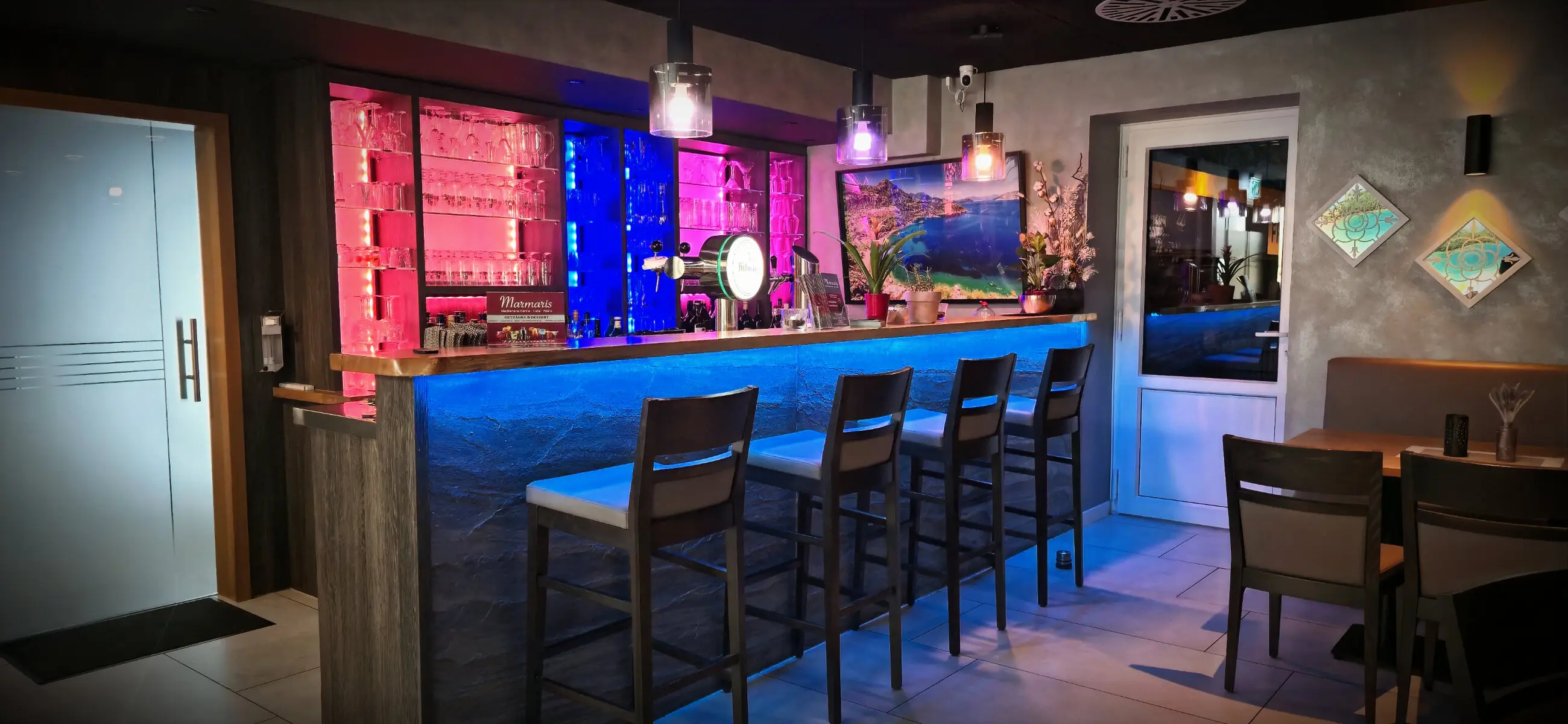 Die beleuchtete Bar im Restaurant Marmaris mit Barhockern und farbigem Licht